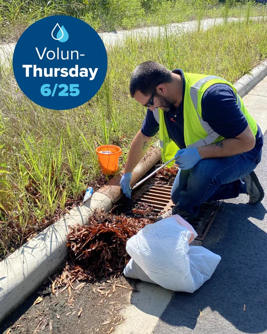 A person wearing a neon safety vest and gloves is cleaning debris from a roadside drain. A white bag and orange bucket are nearby. A blue circle with a water droplet icon reads "Volun-Thursday 6/25.