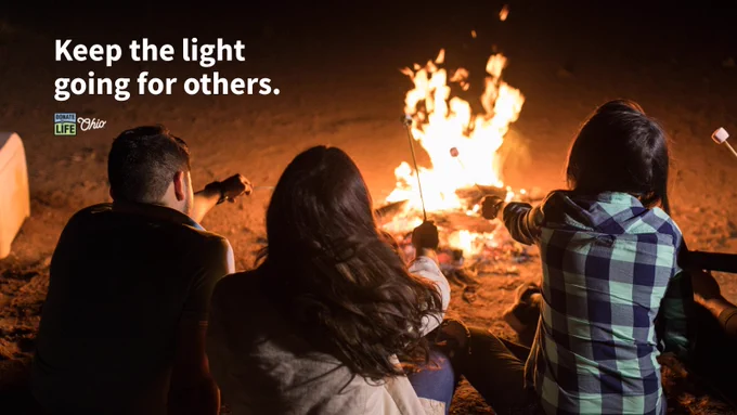 Three people sit around a campfire toasting marshmallows. The text reads: "Keep the light going for others." A "Donate Life Ohio" logo is in the top left corner.