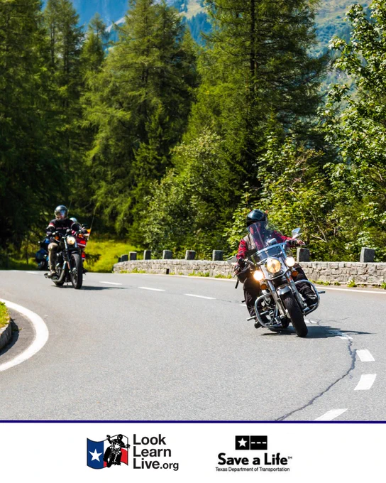 Two motorcyclists riding on a scenic, curved mountain road surrounded by trees. Logos for "Look Learn Live.org" and "Save a Life - Texas Department of Transportation" are visible at the bottom.
