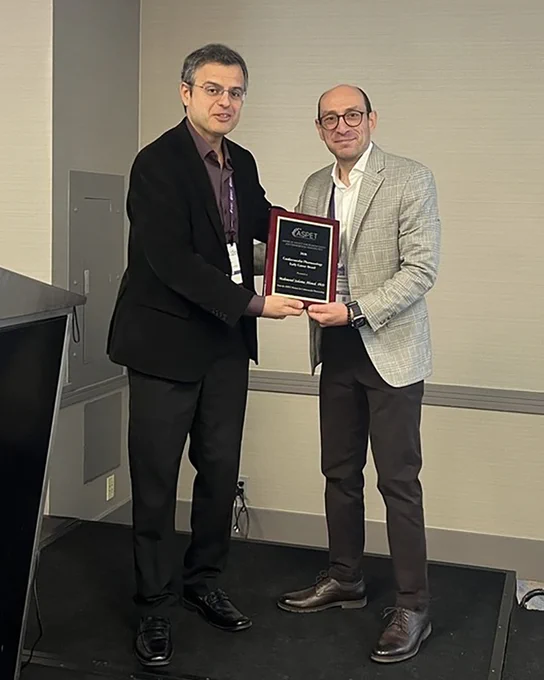 One man hands another an award plaque while standing on stage.