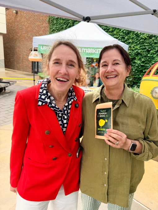 Elizabeth Shaffer smiles for a photo with a woman holding a package of pumpkin seeds at the Uptown Farmers Market.