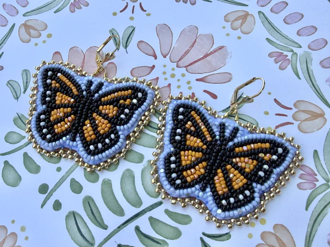 Flat stitched beaded earrings in a monarch butterfly design. Laying on a floral background.