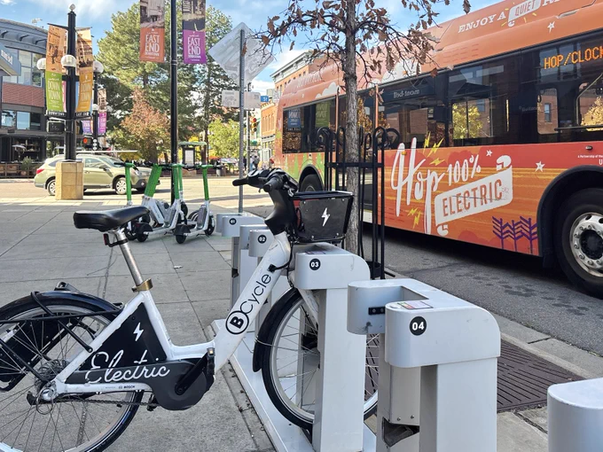 A Bcycle bike attached to a rack in the foreground. Behind it is a bus and cluster of scooters.