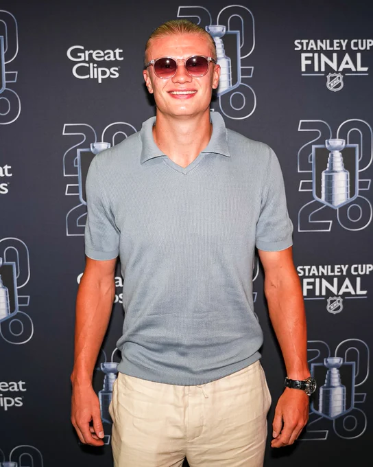 Erling Haaland smiling for a photo in a gray shirt and sunglasses.