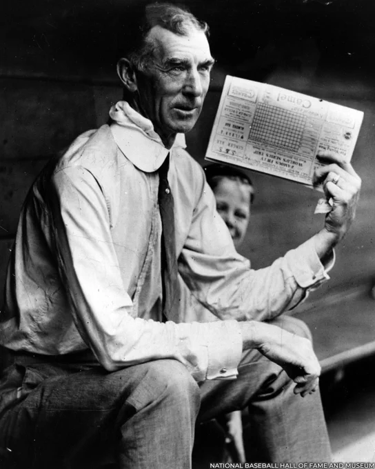 Connie Mack holds up a scorecard while seated in the dugout. (National Baseball Hall of Fame and Museum)