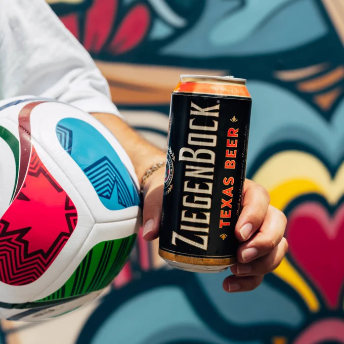 A World Cup soccer match watch party headquarters photo from Karbach Brewing Co. of a person holding a colorful soccer ball and a can of ZiegenBock Texas Beer in front of a vibrant, abstract mural.