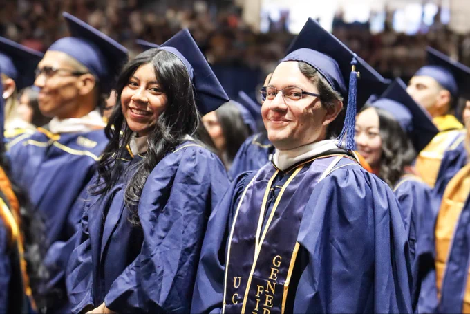 Master's graduates smiling with one wearing a "First Generation" stole.