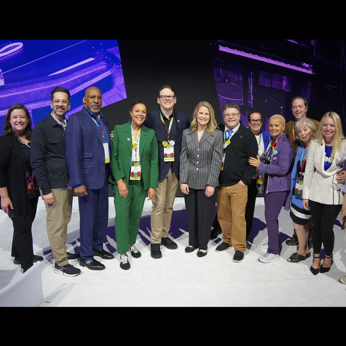 Group of professionals standing together on a stage with a large screen backdrop displaying abstract blue graphics.