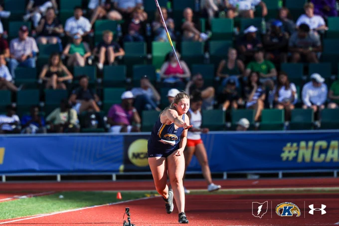 A person in athletic gear is participating in a javelin throw at a track and field event. Spectators are seated in the background. The setting includes banners with the NCAA logo, indicating a collegiate sports event.