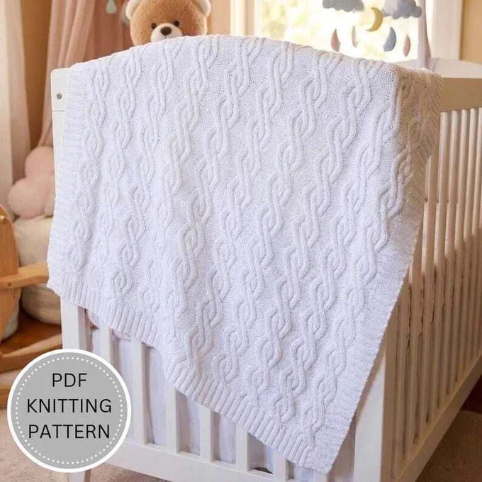 A white cable-knit baby blanket is draped over a white wooden crib. A gray circular badge at the bottom left reads "PDF KNITTING PATTERN." The nursery background includes a teddy bear, pink curtains, a mobile, and a wooden rocking horse.