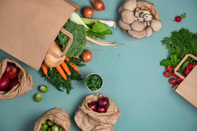 A close up of a blue table topped with bags that hold vegetables.