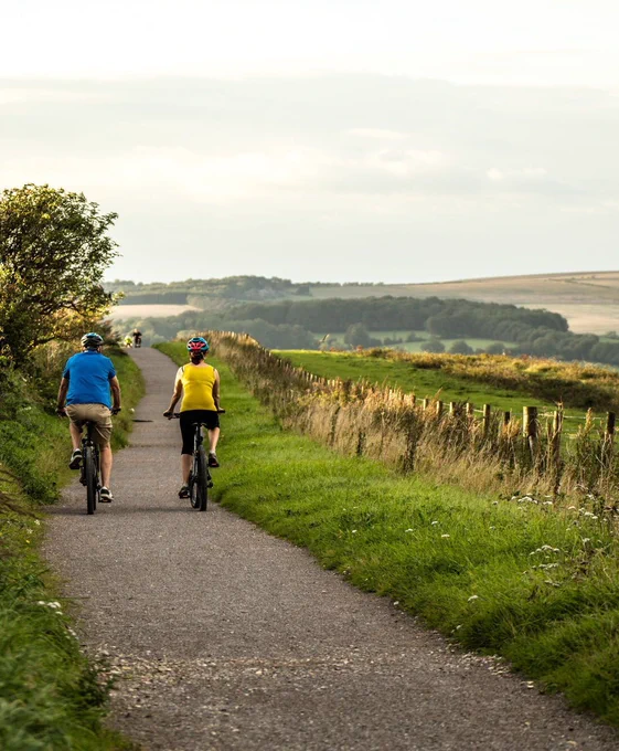 Two cyclists cycling on a gravel path with rolling hills in the distance.