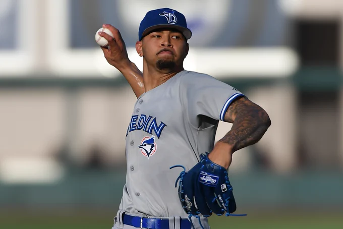 Daniel Guerra winds up to throw a pitch while wearing a blue Dunedin Blue Jays hat and a gray uniform top.