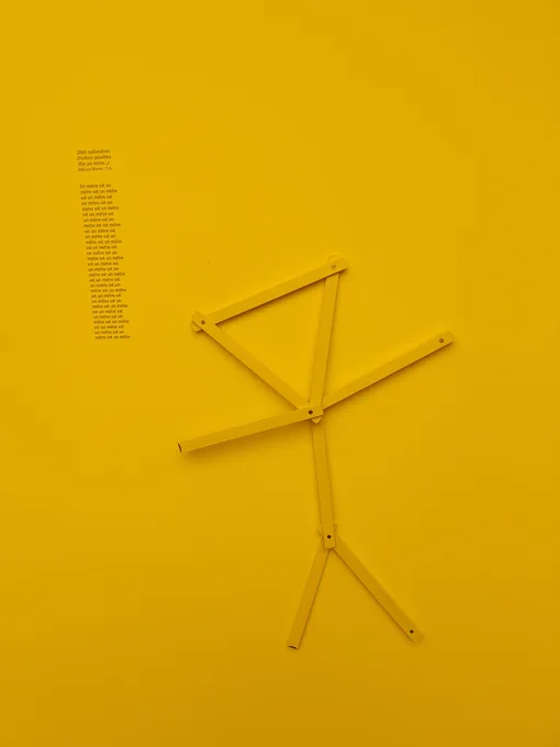 Ein Bereich des Kunstwerks "Sechzigtausend Millimeter unendlicher Möglichkeiten" von Saadane Afif: eine gelbe menschlich anmutende Zollstock-Figur an einer gelben Wand.