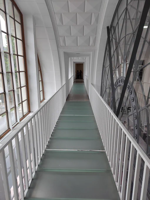 Verglaster Übergang zwischen den Museumsflügeln: auf der einen Seite ist eine  Fensterfront zu sehen, auf der anderen die Zeiger der großen Bahnhofsuhr.