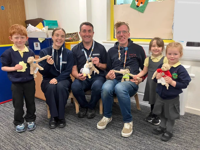 Group of children and adults sitting and standing in a classroom, each holding small stuffed animal toys.