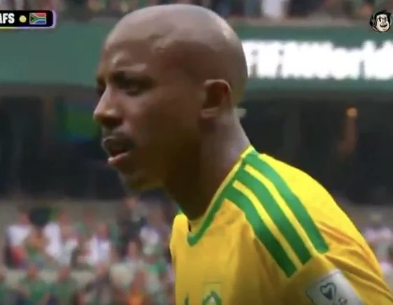 A frustrated athlete in a yellow jersey, with green stripes, stands on a soccer field amidst a cheering crowd.
