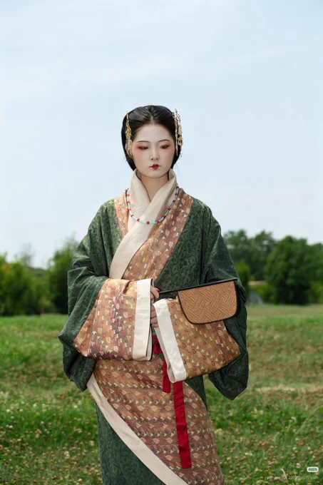 Woman in Han dynasty hanfu, dark green with copper and cream borders. Hair pinned back. In a park.