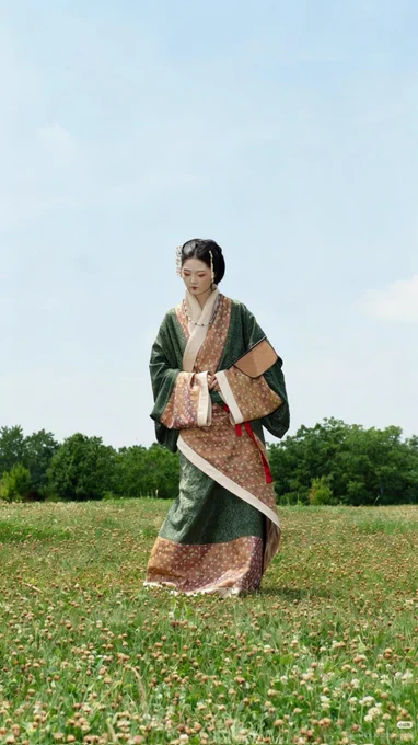 Woman in Han dynasty hanfu, dark green with copper and cream borders. Hair pinned back. In a park.