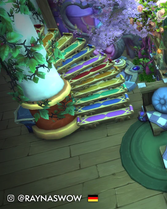 Die Innenansicht des Hauses eines World of Warcraft-Spielers, mit Holzb\u00F6den, Holzw\u00E4nden und Holzm\u00F6beln. Eine elegante Wendeltreppe schlingt sich um eine zentrale, belaubte S\u00E4ule. Die einzelnen Stufen sind der Reihe nach in den Farben des Regenbogens gef\u00E4rbt - Lila, Blau, Gr\u00FCn, Gelb, Orange, Rot; sich danach wiederholend. Die Treppe verschwindet hinter der S\u00E4ule aus dem Blickfeld. Um sie herum wachsen mehr Pflanzen in Gr\u00FCn-, Pink- und Lilat\u00F6nen. Der Text am unteren Rand benennt den Baumeister als Instagram-Nutzer Raynaswow aus Deutschland.
