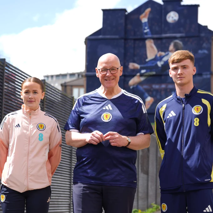 First Minister John Swinney in front of the Scott McTominay mural in Glasgow with two youth footballers. 