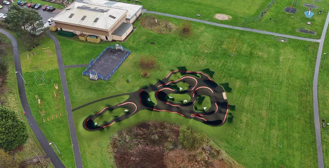 Aerial view of a new pump track with illuminated red edges, surrounded by grass