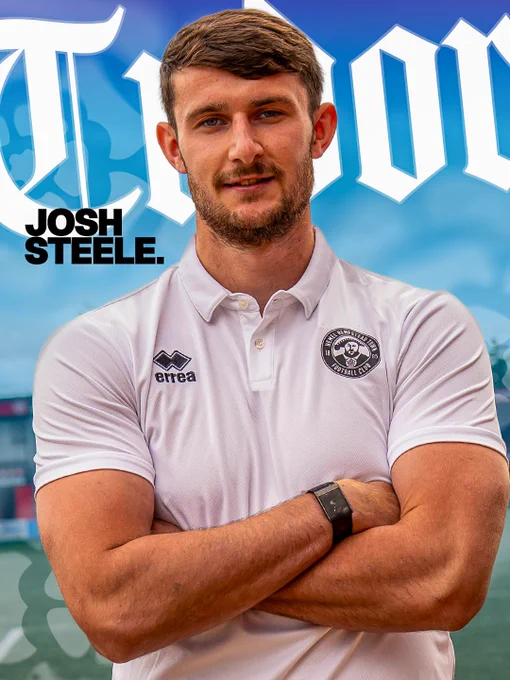 Josh Steele in a Hemel FC white polo shirt stands with arms crossed against a blue sky background.