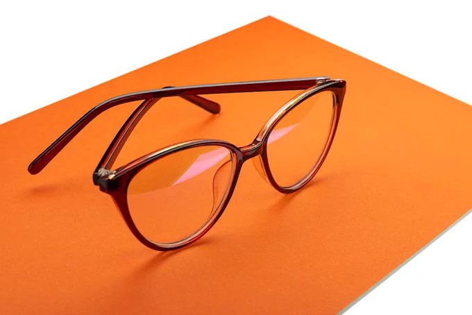 Close-up view of trendy eyewear with brown frames placed on an orange background, showcasing elegant design.