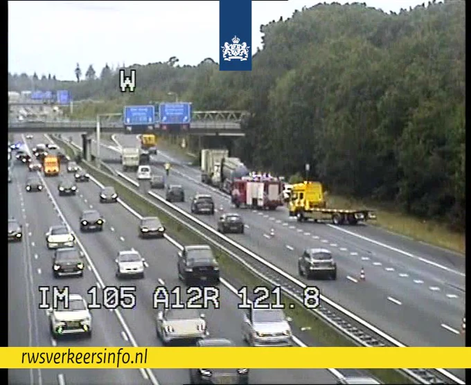 Verkeer rijdt over één rijstrook langs een ongeval. Brandweer, berger en politie staan op de afgesloten rijstroken. Ook staan de betrokken voertuigen daar.