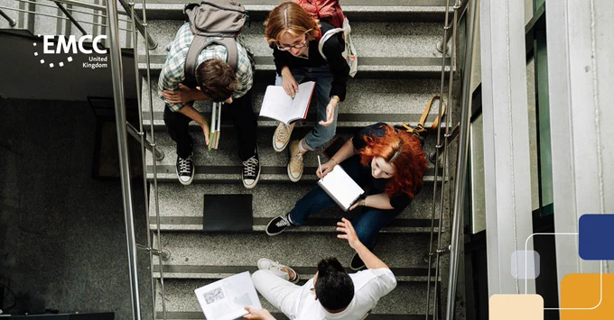 Four students sitting on stairs engaged in discussion with notebooks and papers.