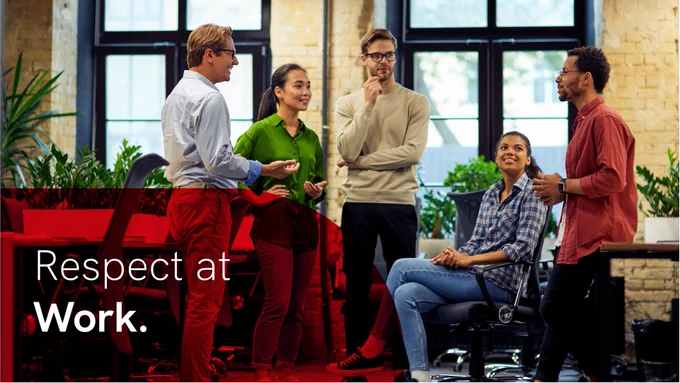 Five diverse colleagues in an office space, they are stood and sat closely together and are engaged in a friendly conversation. In the bottom left corner is a red overlay with white text reading: 'Respect at Work.'