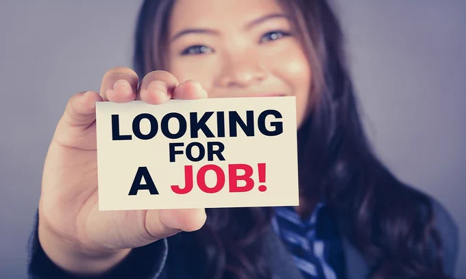 Person holding a card that says 'LOOKING FOR A JOB!' with emphasis on the word JOB in red letters.