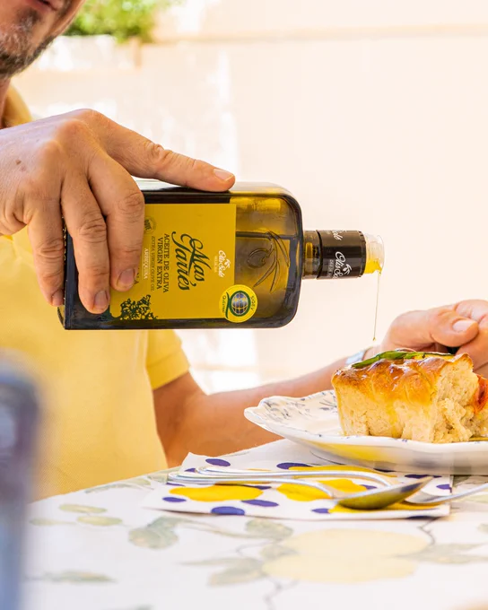Mano vertiendo aceite de oliva de una botella sobre un trozo de pan en un plato