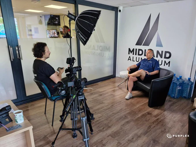 A camera crew prepares to interview a person in an office. The setting is professional, with cameras and lighting equipment visible.