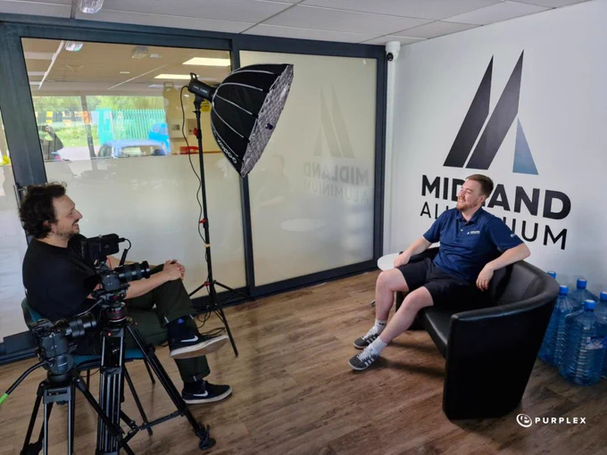 A candid scene showing an interview setup in an office environment. One participant is seated in a chair while the other is behind a camera, suggesting a professional context.