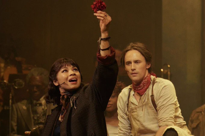 A photo showing a woman holding a flower as a man looks bemused, both on a stage 