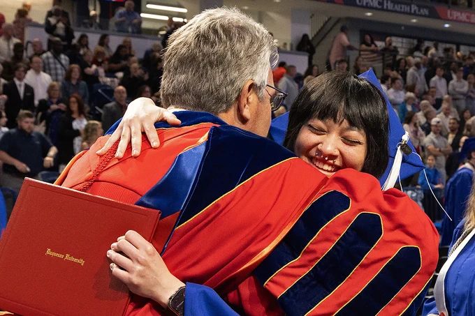 Malka gets a hug from President Gormley after receiving her diploma on stage. She has a big smile on her face.