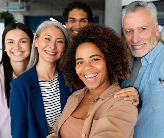 Diverse group of five people standing close together in a building, smiling and wearing professional casual clothes.
