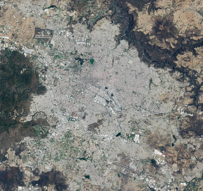 Landsat 8 satellite image of Guadalajara, Mexico. The sprawling gray city dominates the image and is surrounded by grids of farmland and dark mountain ranges.