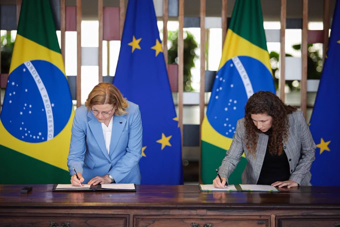 EVP Henna Virkkunen and Minister Esther Dweck sign documents at a formal ceremony in front of Brazilian and European Union flags.