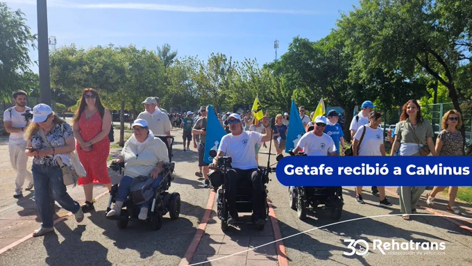 Personas caminando y en sillas eléctricas en una marcha inclusiva con banderas bajo el sol en Getafe.