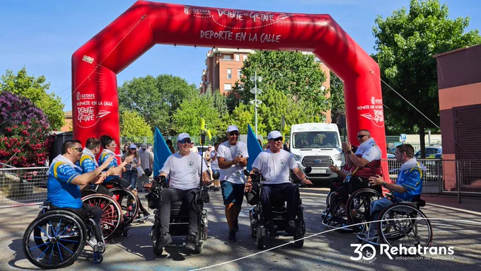 Personas en silla de ruedas celebrando bajo un arco rojo con texto "Deporte en la calle".