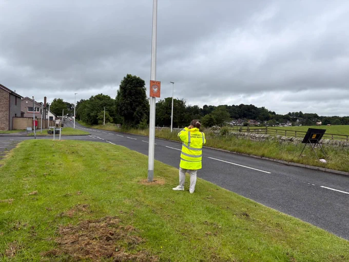 Community Speed Watch volunteer monitoring traffic on a road with a speed gun.