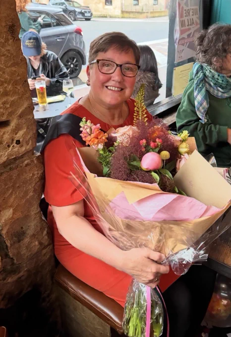 Ann is smiling, sitting with a bouquet of flowers from SCOSLI