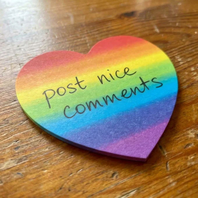 A colorful heart-shaped card with the text "Post nice comments" written on it against a wooden background.