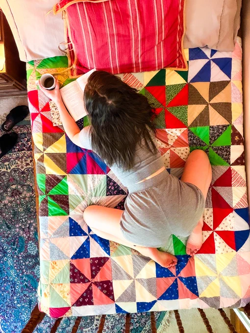 a brunette on her bed crouched over a book, coffee in hand