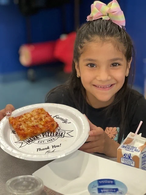 Student eats slice of pizza and smiles