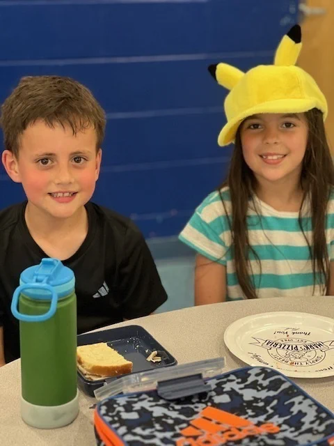 students at a table with a sandwich and Pikachu hat pose for a photo 
