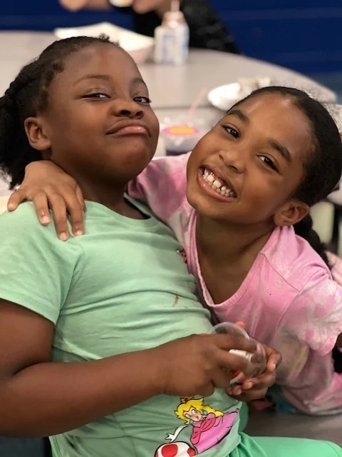 students smile and laugh for a picture in the lunchroom wearing green and pink shirts