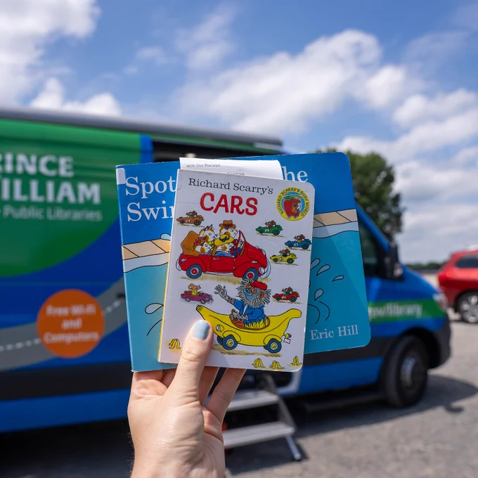 Richard Scarry's "Cars" and another board book behind it are held up in frame in front of PWPL's Mobile Library.